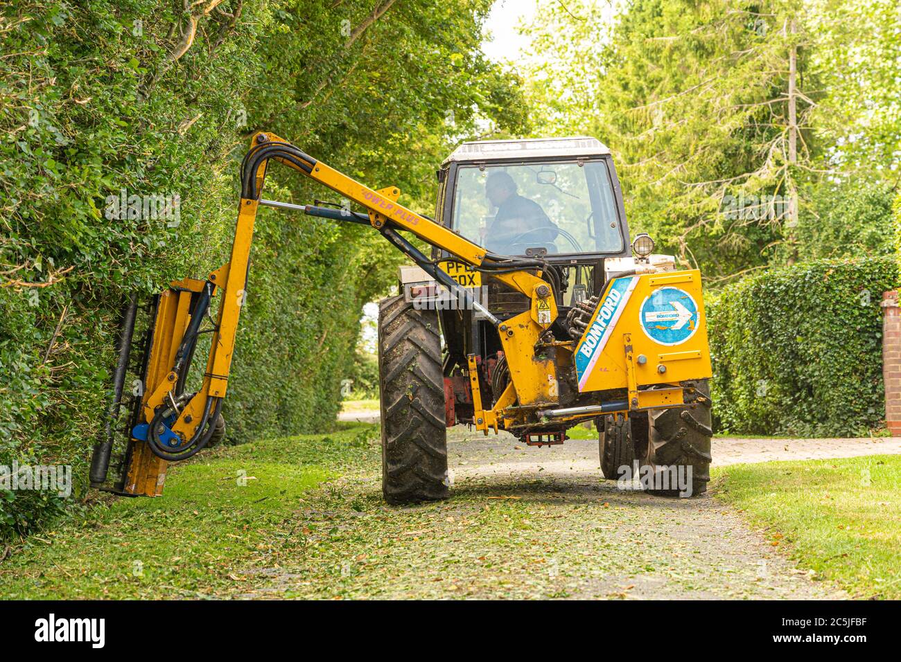 Rear view of man in a tractor using a flail hedge cutter to cut hedges in a country lane. Much Hadham. Front view version available in my portfolio. Stock Photo