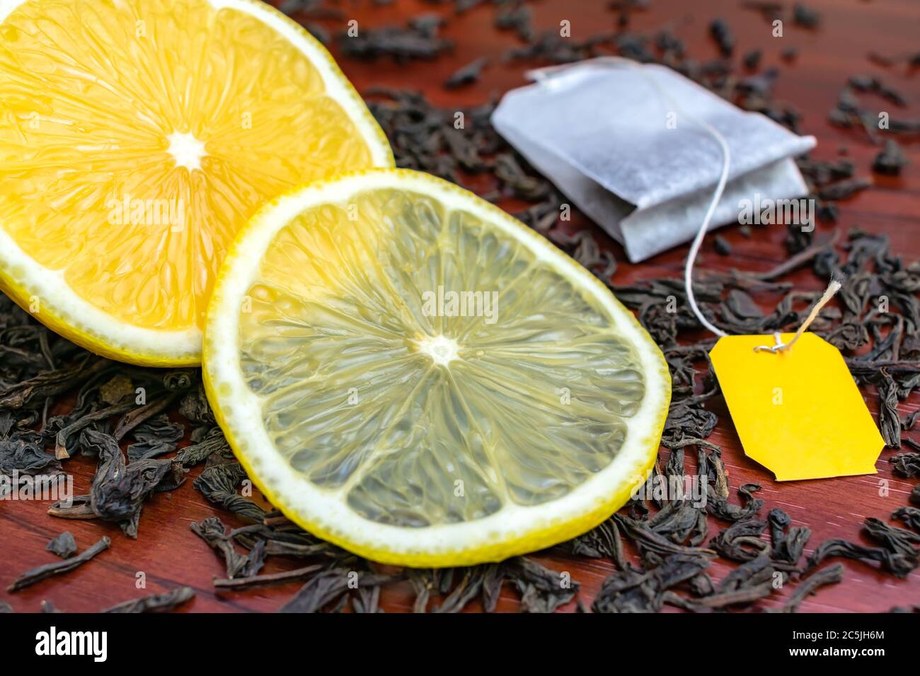 A cut juicy lemon lies on the leaves of black tea with a tea bag Stock