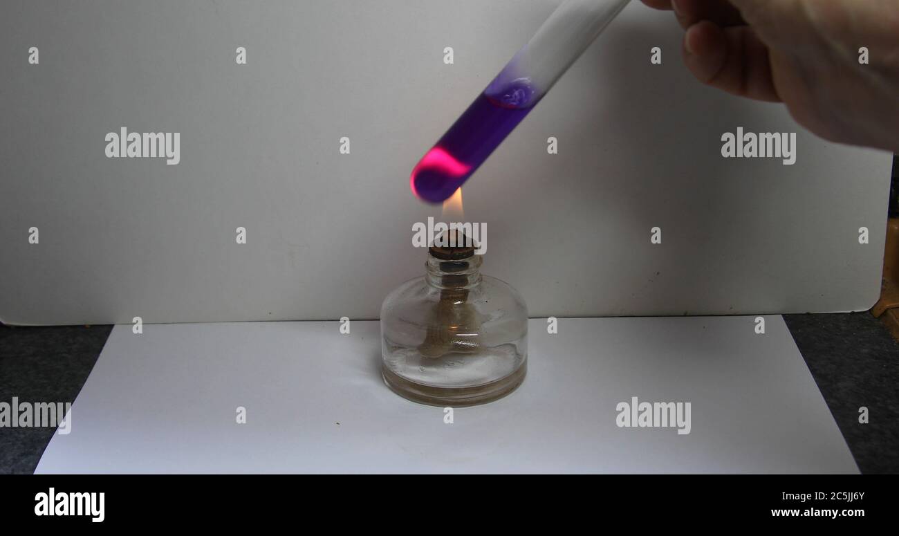 Hand holds test tube with blue liquid over a flame of alcohol burner Stock Photo