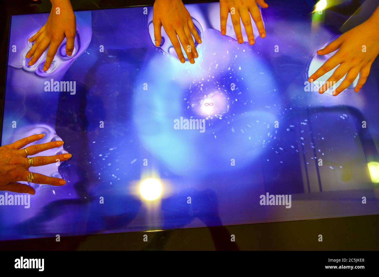 Many hands of young girls playing over big blue touch screen with infinite sign in the centre,  making blue color bubbles Stock Photo