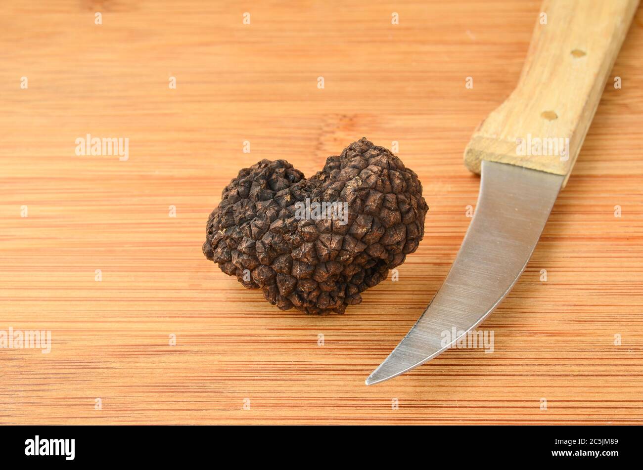 Heart shaped Black truffle and knife on wooden background Stock Photo