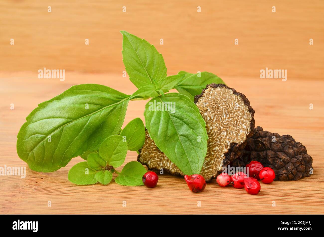 Black truffle cut on half on wooden background, with basil, oregano and red pepper Stock Photo