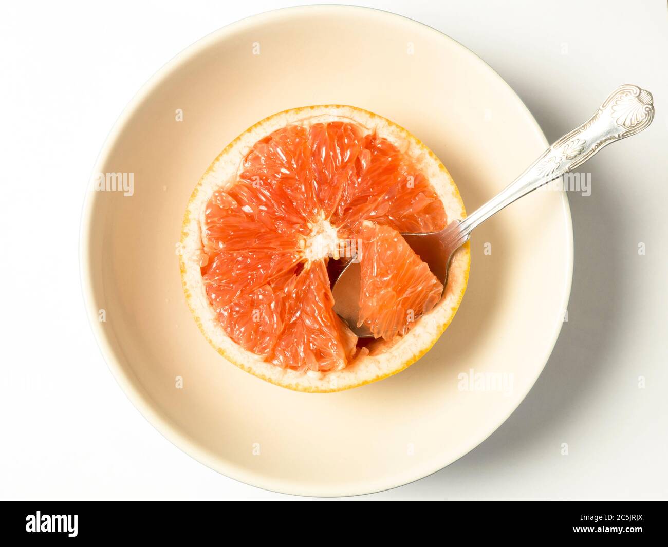 Half a pink grapefuit with one segment being removed on a spoon in a bowl centred on a white background Stock Photo