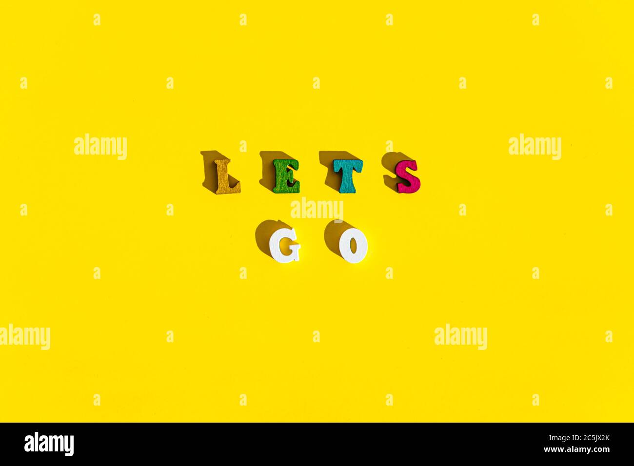 Flatlay of wood multicolored letters is inscription of lets go with shadows on bright plain yellow background. wishes and messages made up of models Stock Photo