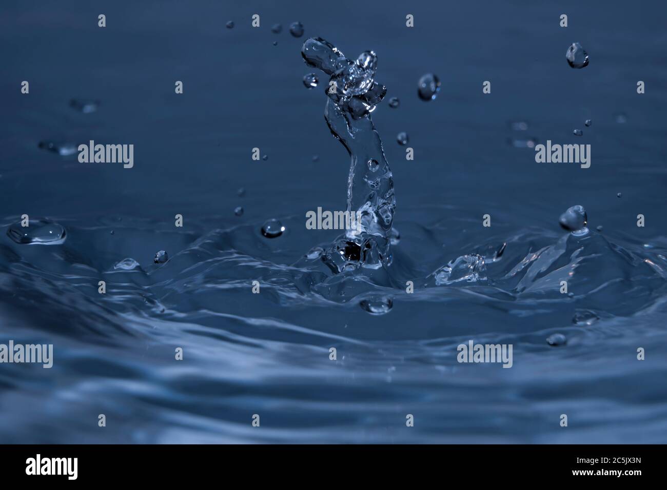 Splashing water drops causing wavy water surface and water column Stock Photo