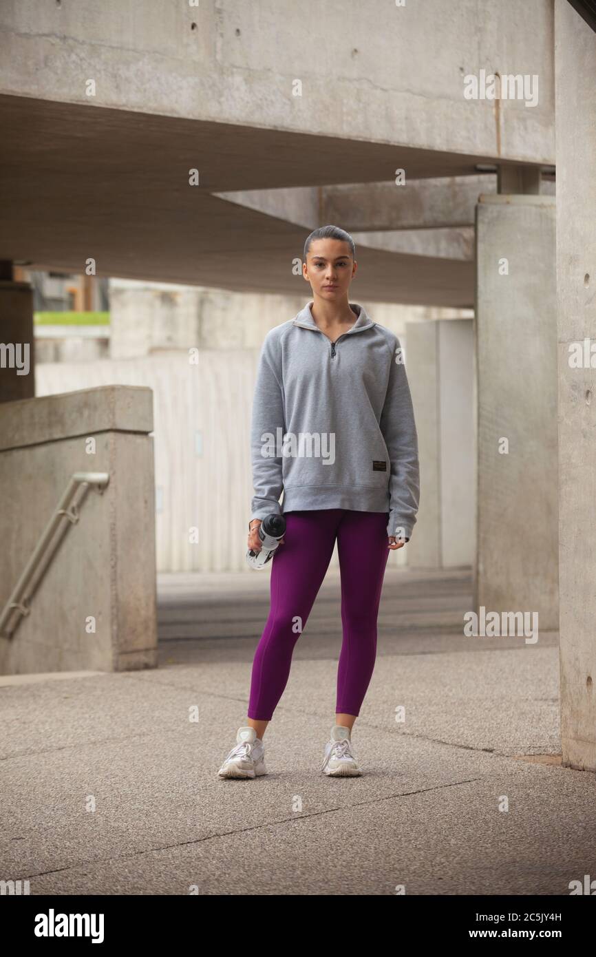 A woman standing wearing purple leggings, grey sweatshirt and