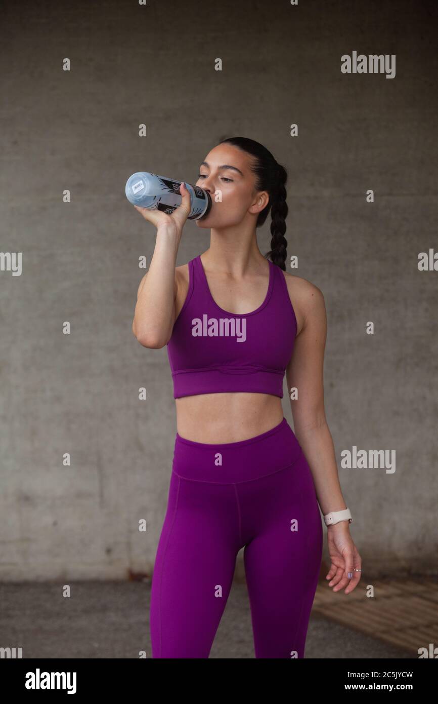 Woman wearing leggings and sports bra drinking from a plastic sports water bottle. Stock Photo