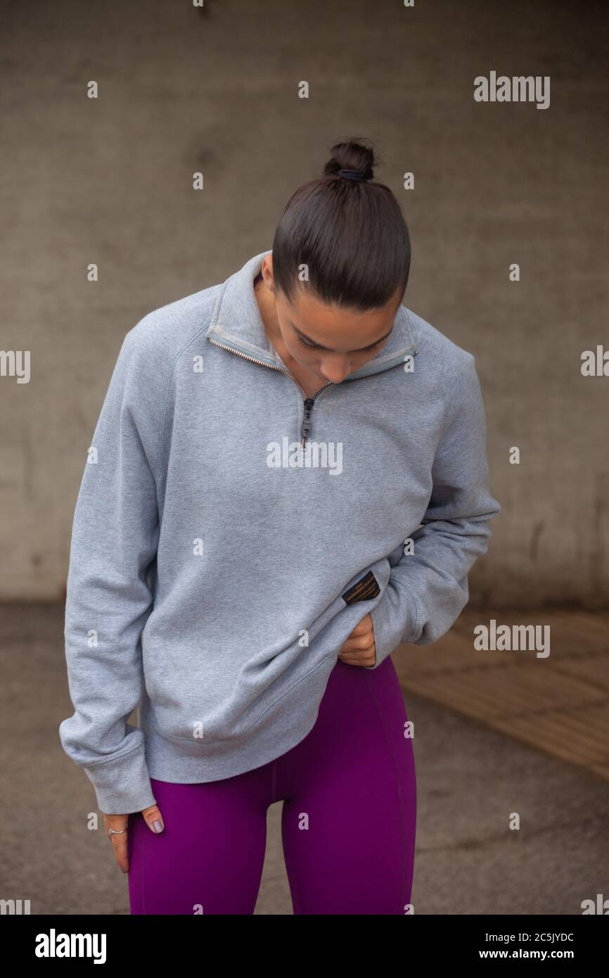 A young woman lifting her sweatshirt to reveal purple leggings Stock Photo