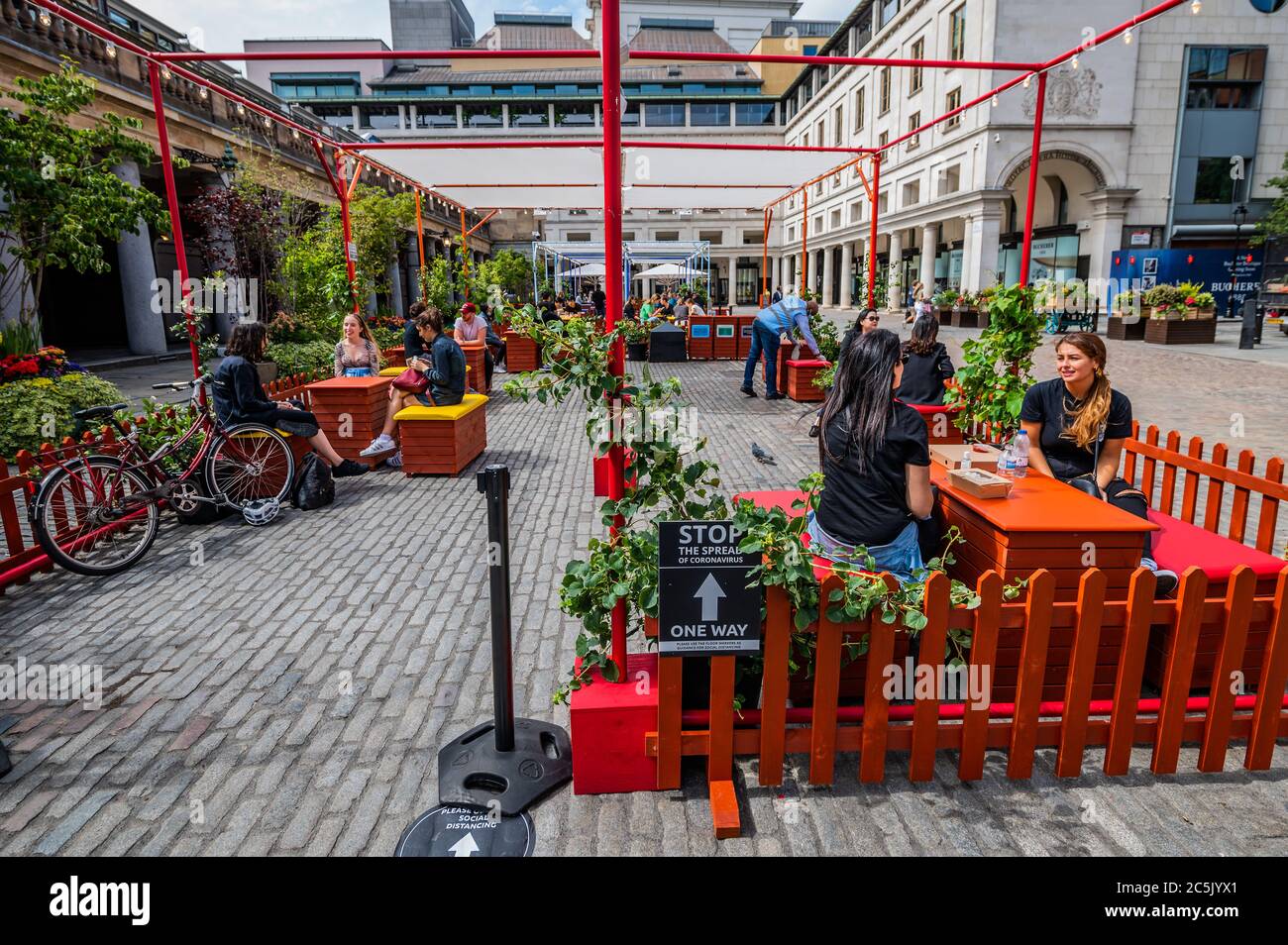 London, UK. 03rd July, 2020. People are already having fun in the communal alfresco seating area - Covent Garden prepares for the new re-opening on July $th (tomorrow) with signage and hand sanitiser - albeit many places are already open, if only partially. The city opens up following the easing of Coronavirus (COVID-19) lock-down. Credit: Guy Bell/Alamy Live News Stock Photo