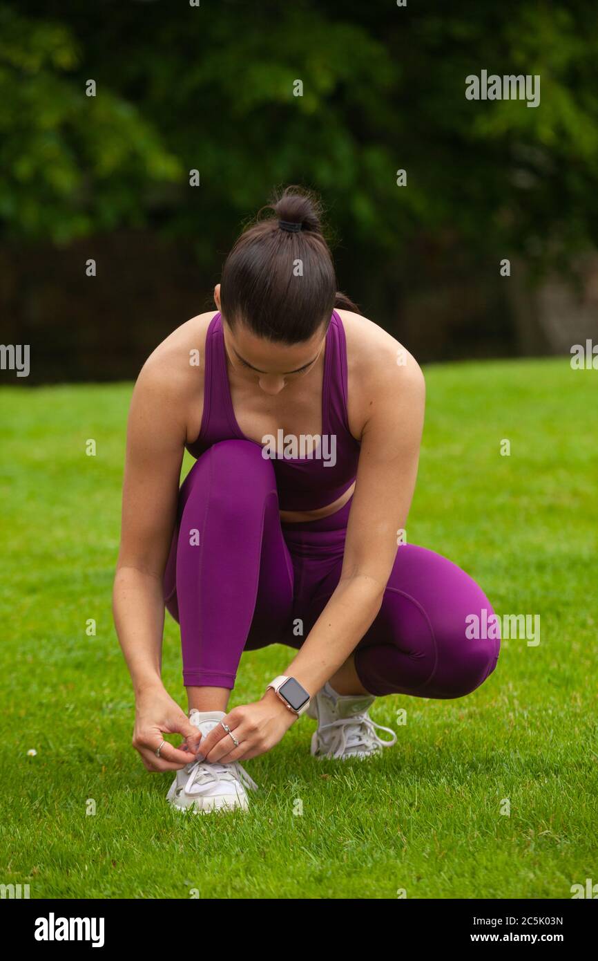 An attractive woman wearing sportswear crouching down on grass and Tying her Shoelace Stock Photo