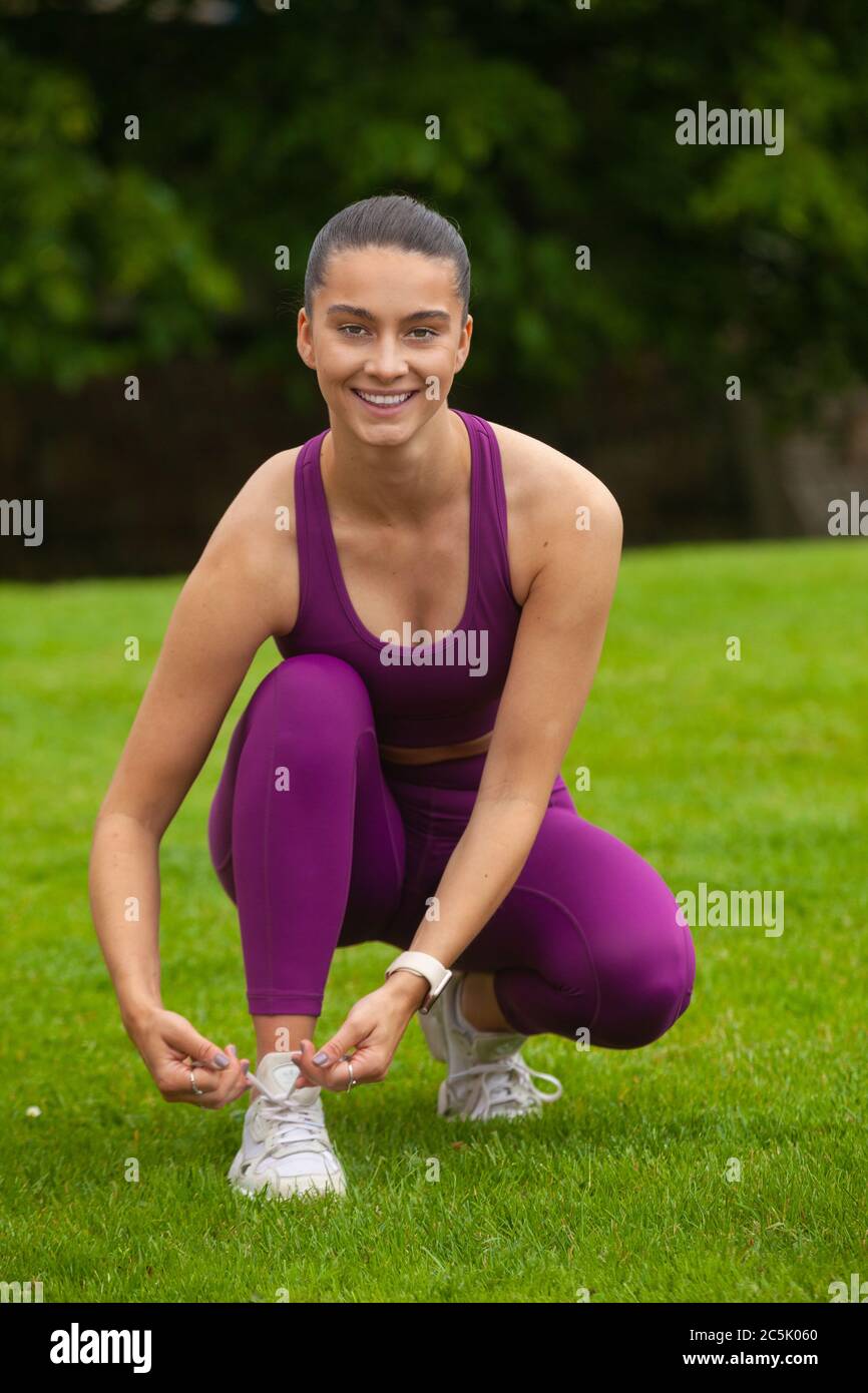 An attractive woman wearing sportswear crouching down on grass and Tying her Shoelace Stock Photo