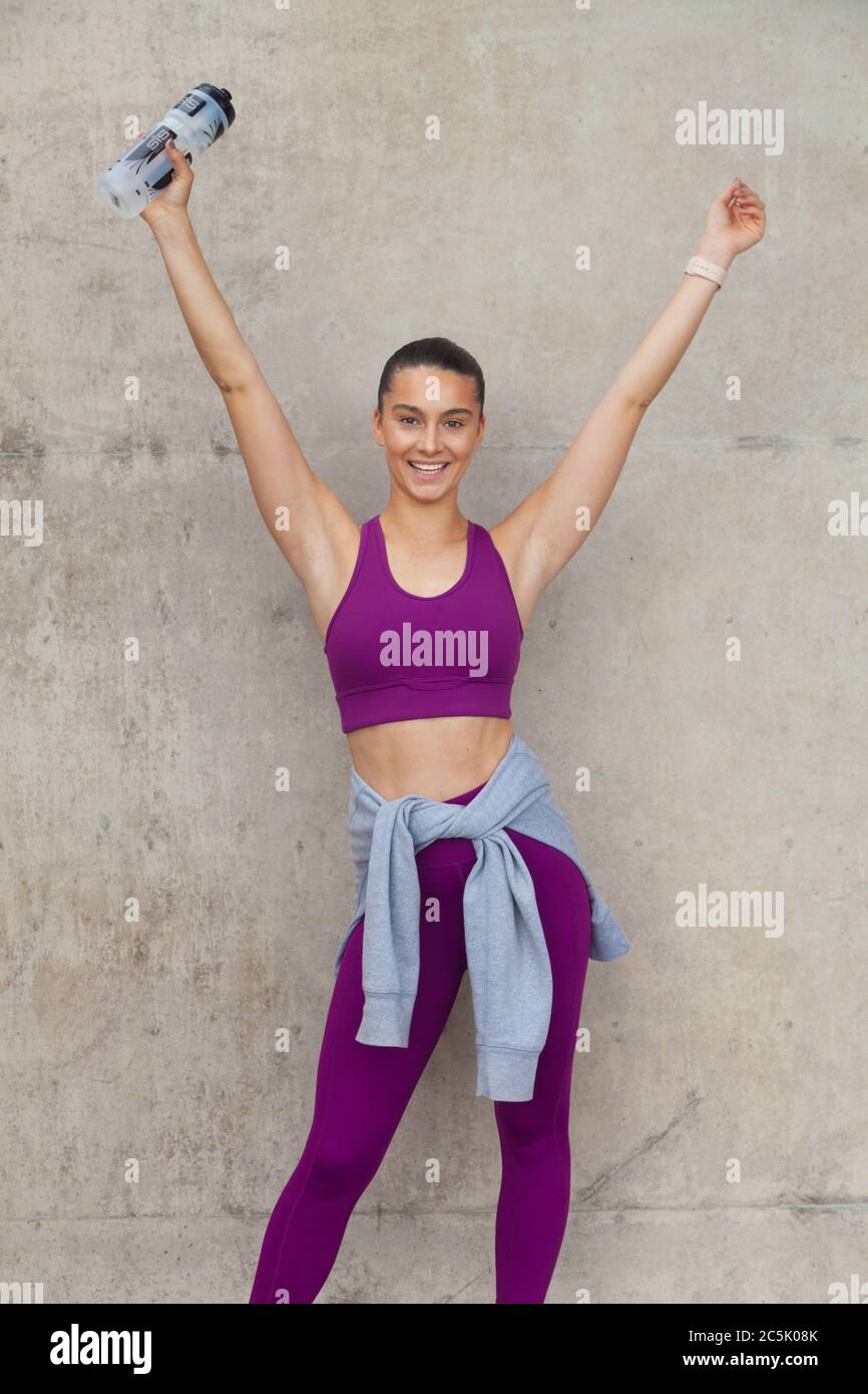 Woman wearing leggings and sports bra with both arms raised in the air Stock Photo