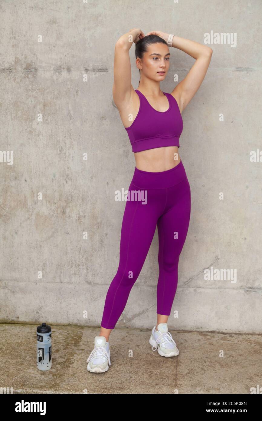 Woman wearing leggings and sports bra with her arms raised near her head Stock Photo
