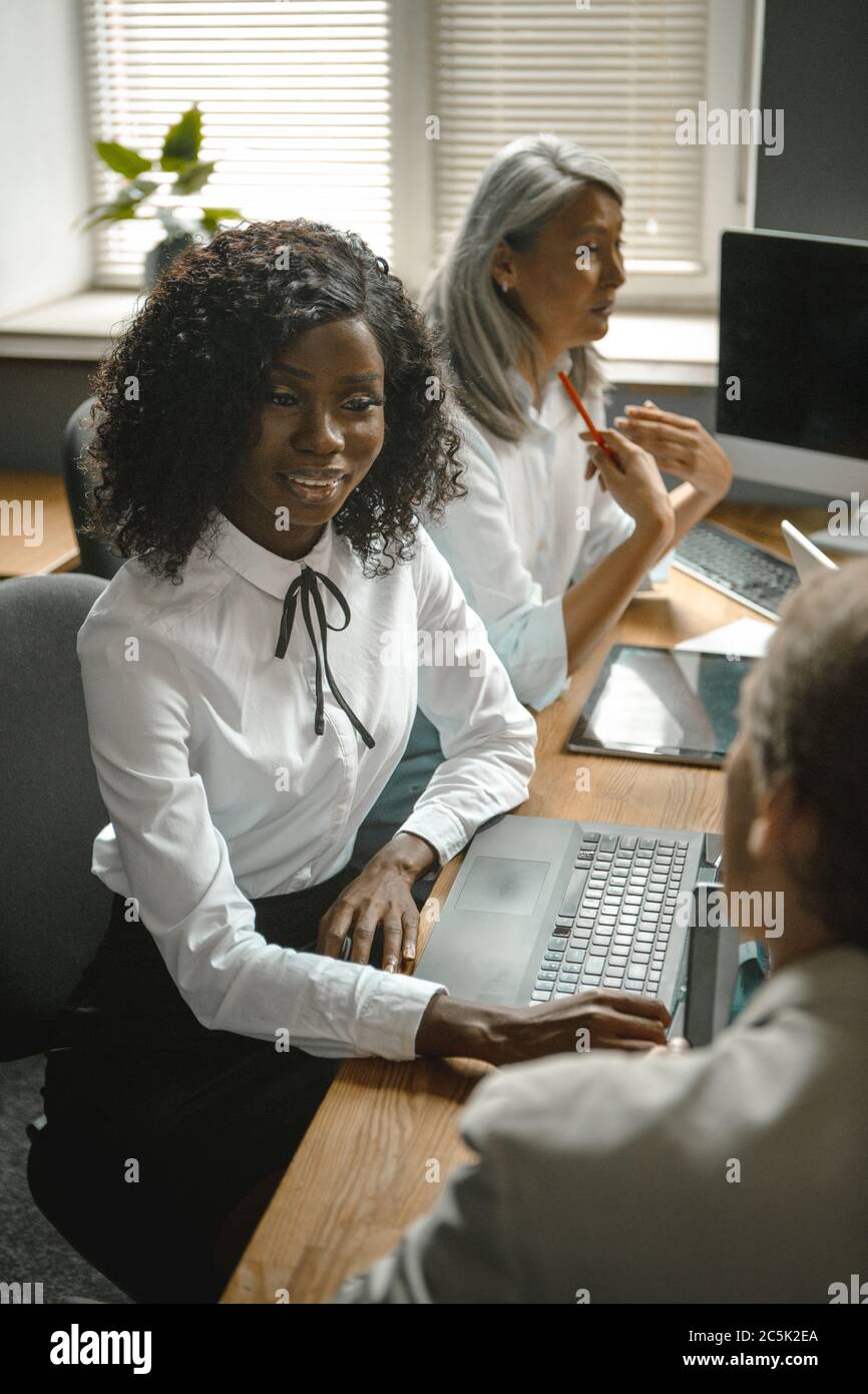 Pretty African young woman communicates with her male colleague sitting at desk. Business people team work in office. Toned image Stock Photo