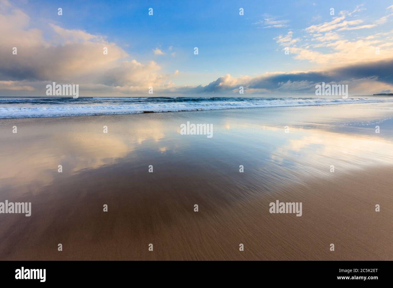 After the stormy sunrise on the coast the last of the threatening clouds begin to soften the light & create mirror like reflections on the beach sand. Stock Photo
