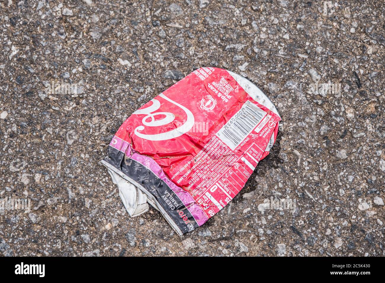 Smashed and crumpled empty Coca-Cola can laying on the ground in the street dumped carelessly polluting the environment Stock Photo