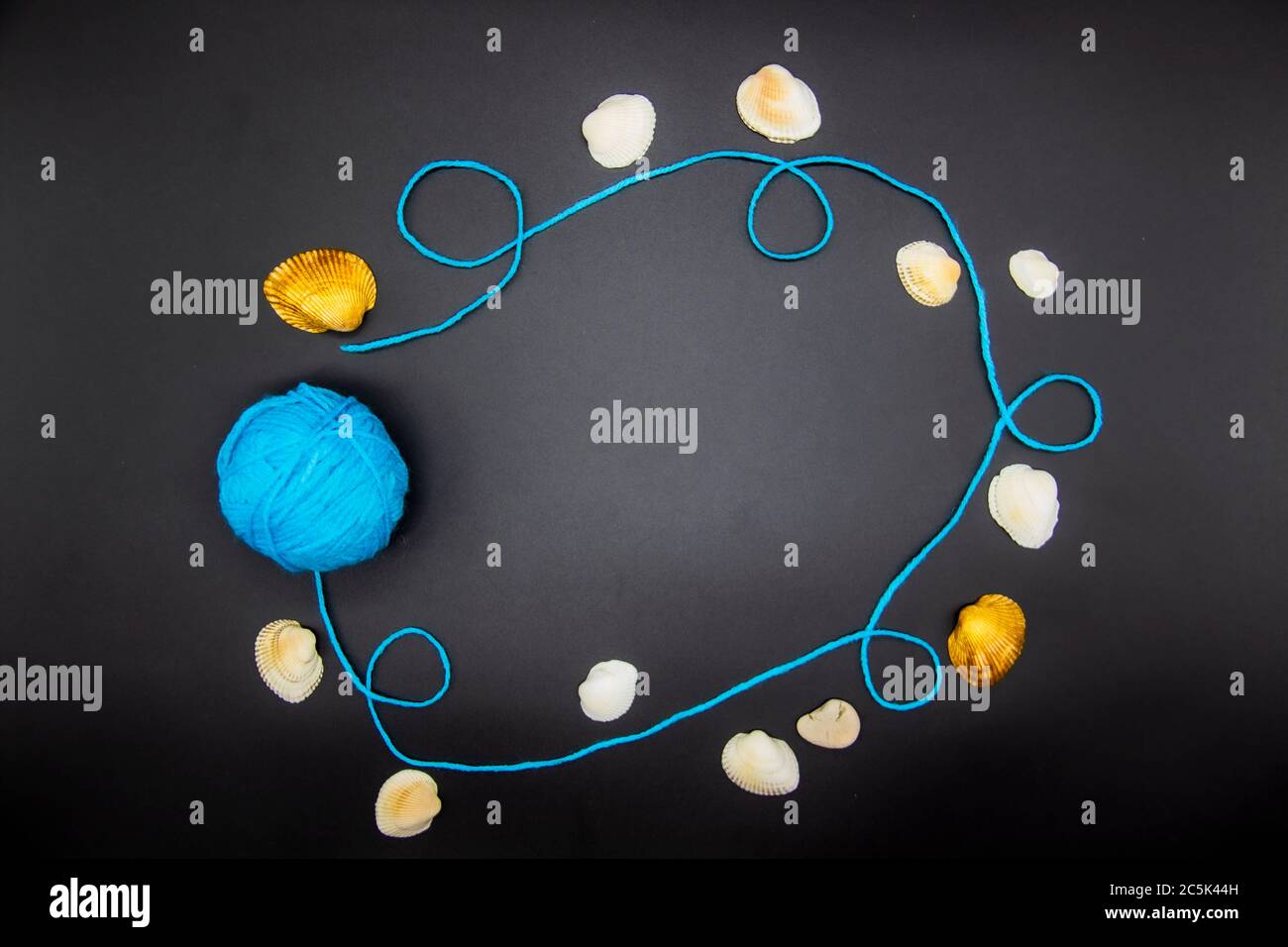 Frame with threads and shells on a black background. A blue skein of ...