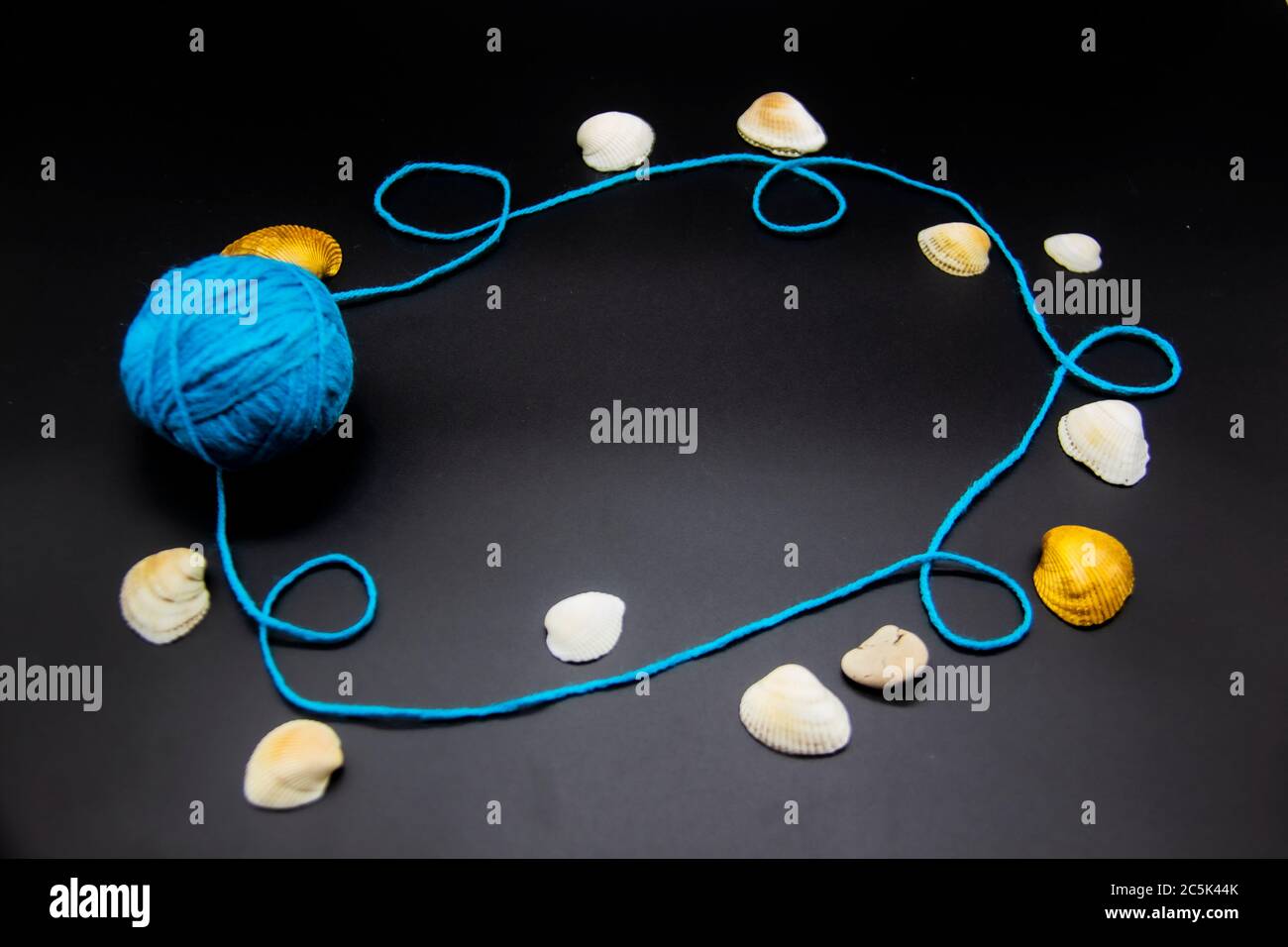 Frame with threads and shells on a black background. A blue skein of ...