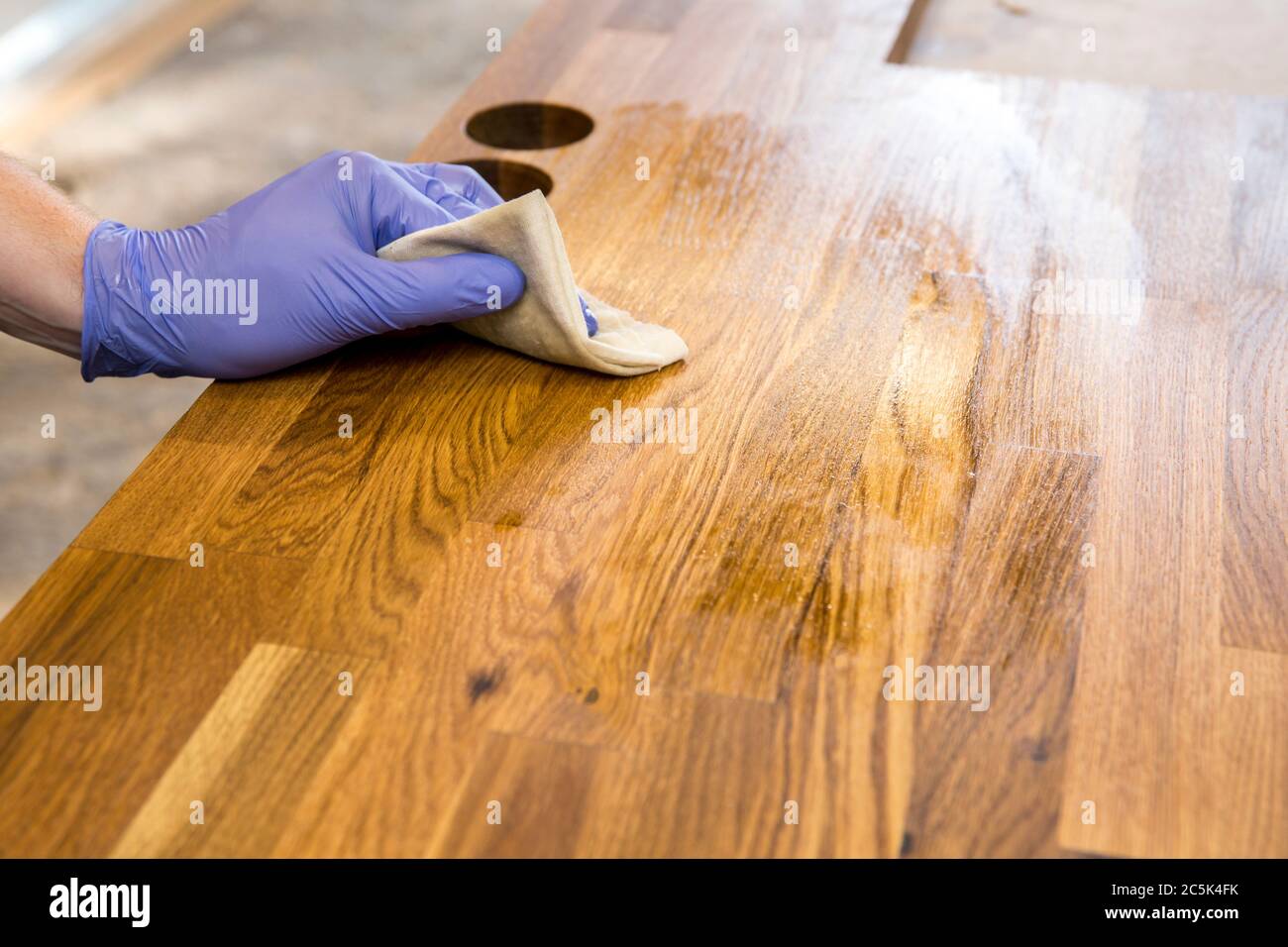Person working, rubbing oiling with linseed oil natural wooden kitchen countertop before using. Solid wood butcherblock countertop maintenance concept Stock Photo