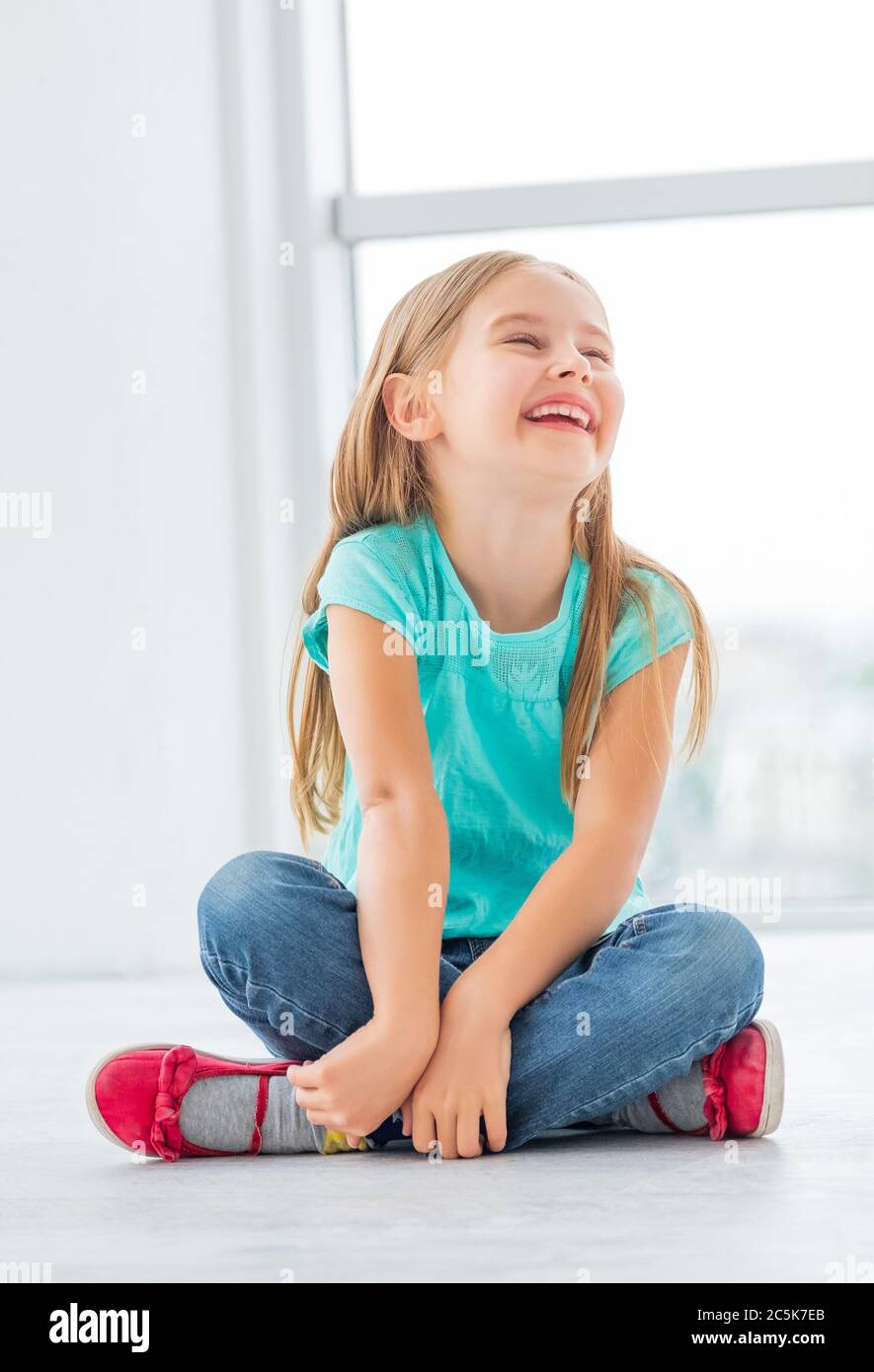 Blonde laughing little girl sits in light room Stock Photo - Alamy