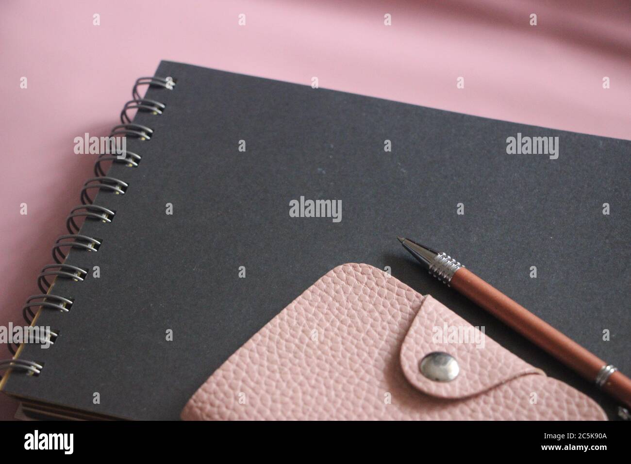 Workspace with spiral copybook, pink leather wallet, and pen. Business ...