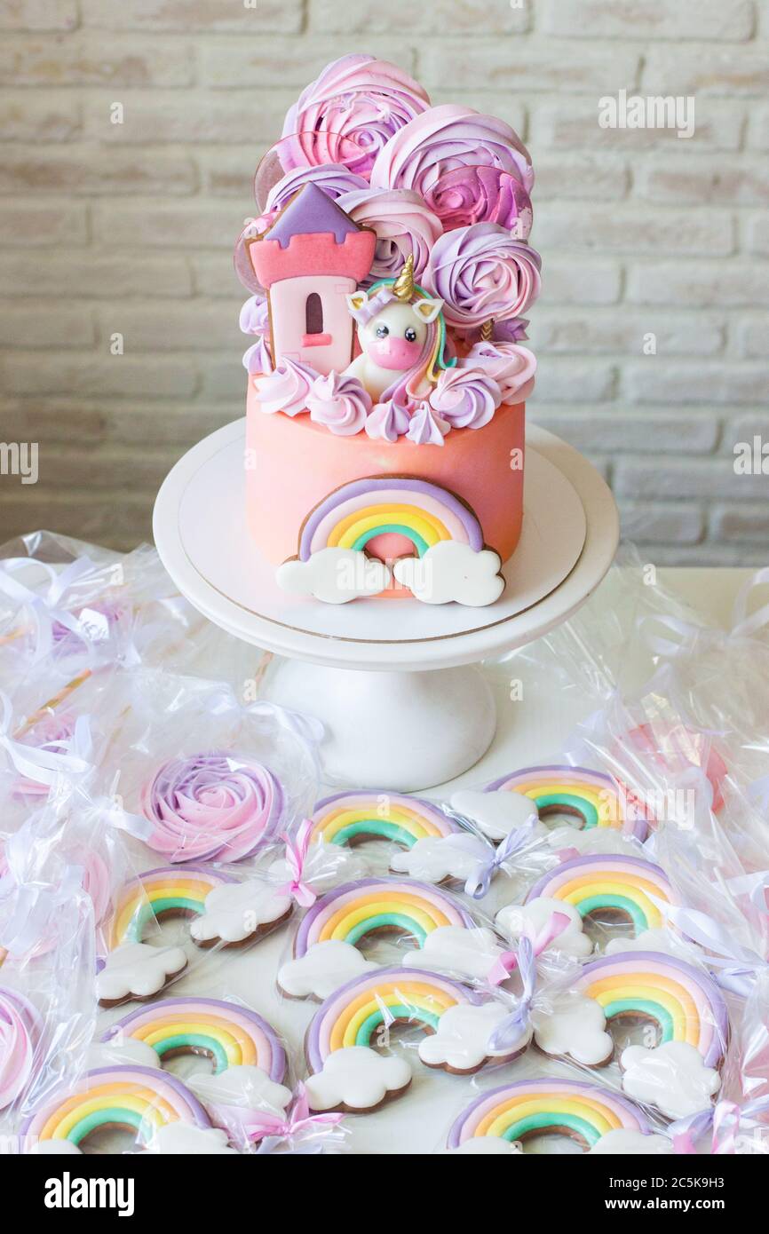 Pink birthday cake with fondant unicorn, rainbow and meringue clouds. Candy bar with cake, cookies and lollipops. Stock Photo