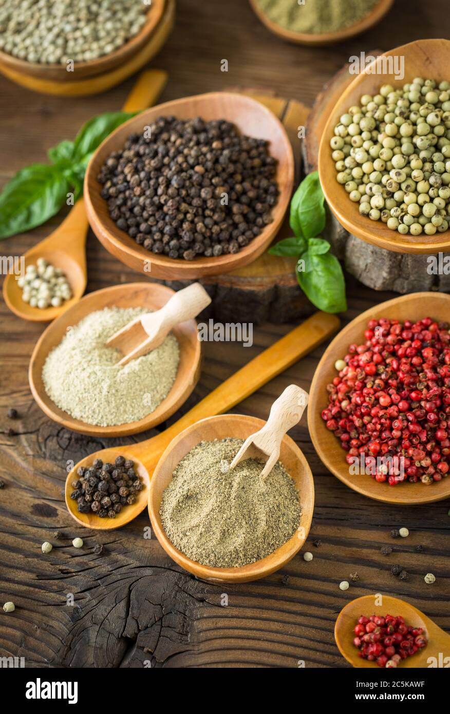Various colorful peppercorns in the bowls and spoons on wooden table. Stock Photo