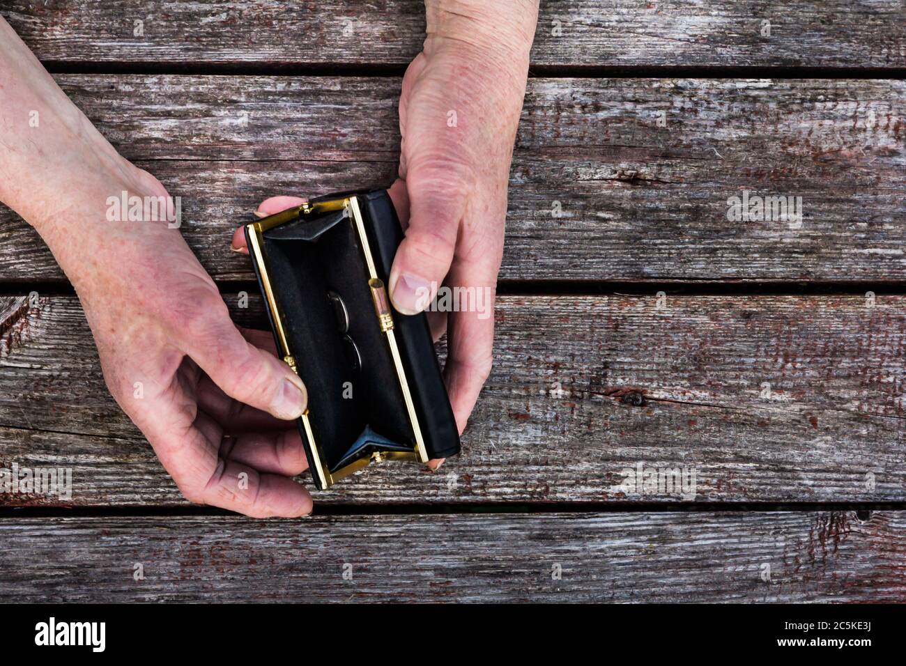 symbol of poverty and financial crisis, two senile hands are holding an empty wallet on a wooden background Stock Photo