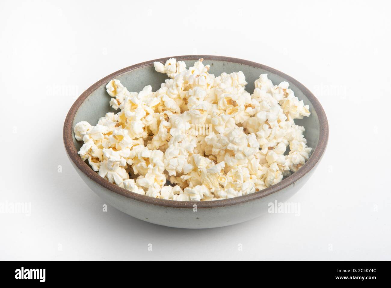 Popcorn in a ceramic bowl set on a plain white background. Stock Photo