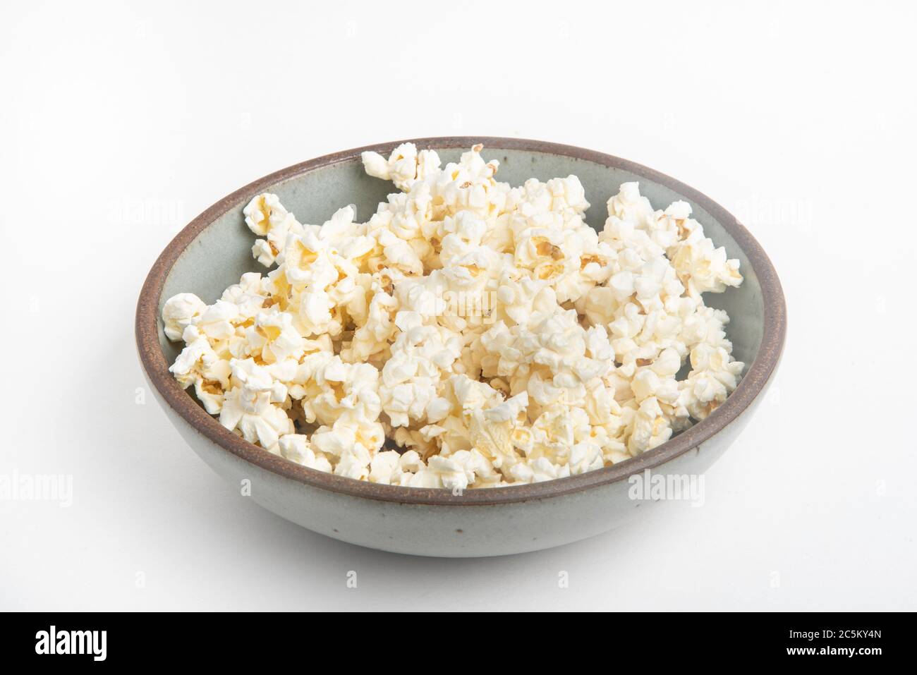 Popcorn in a ceramic bowl set on a plain white background. Stock Photo