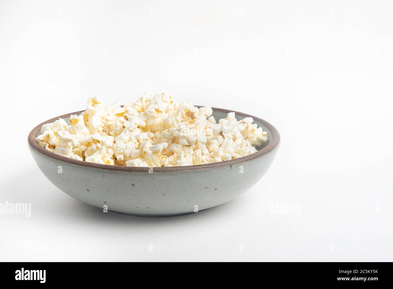 Popcorn in a ceramic bowl set on a plain white background. Stock Photo