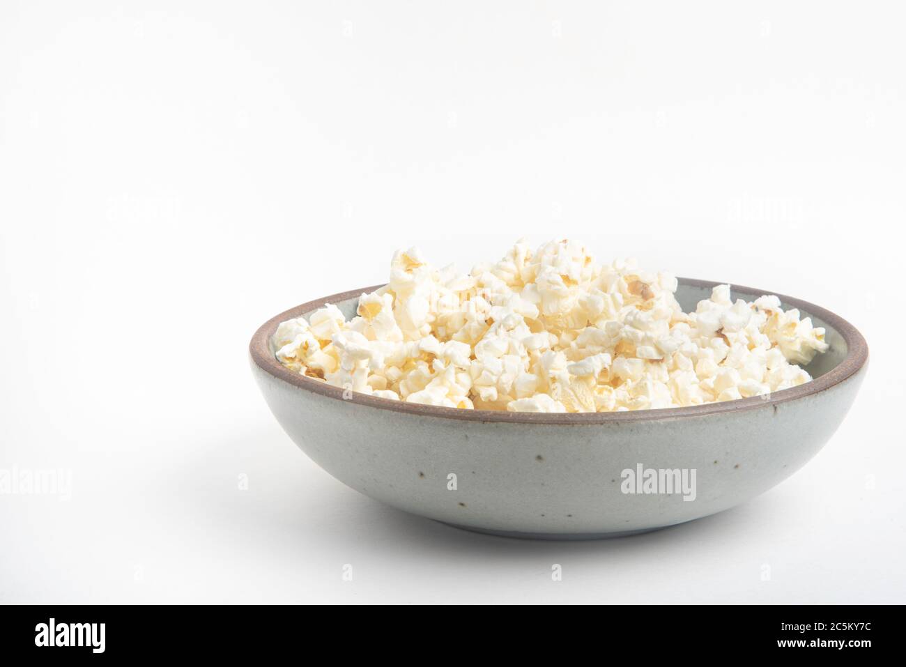 Popcorn in a ceramic bowl set on a plain white background. Stock Photo