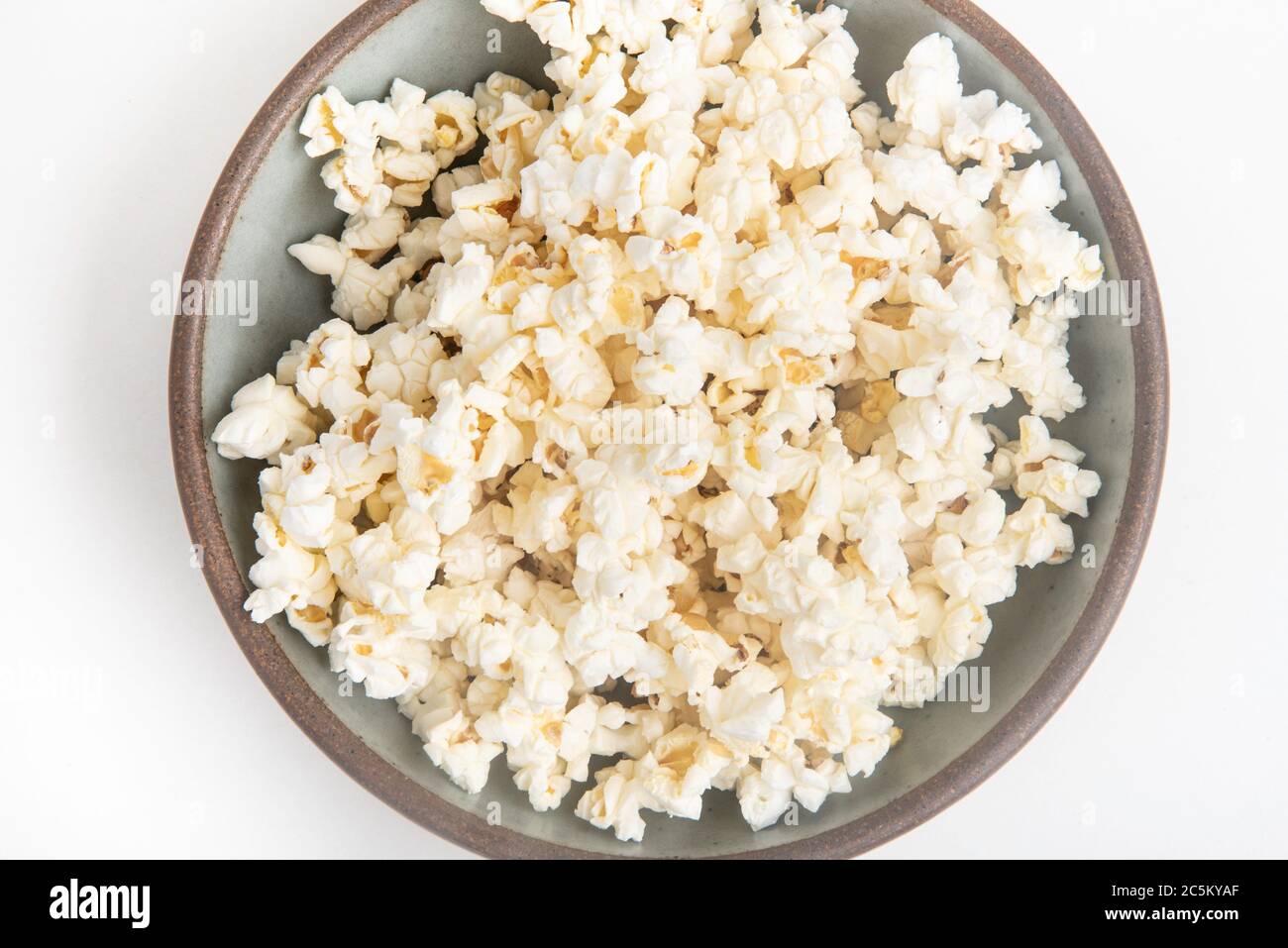 Popcorn in a ceramic bowl set on a plain white background. Stock Photo