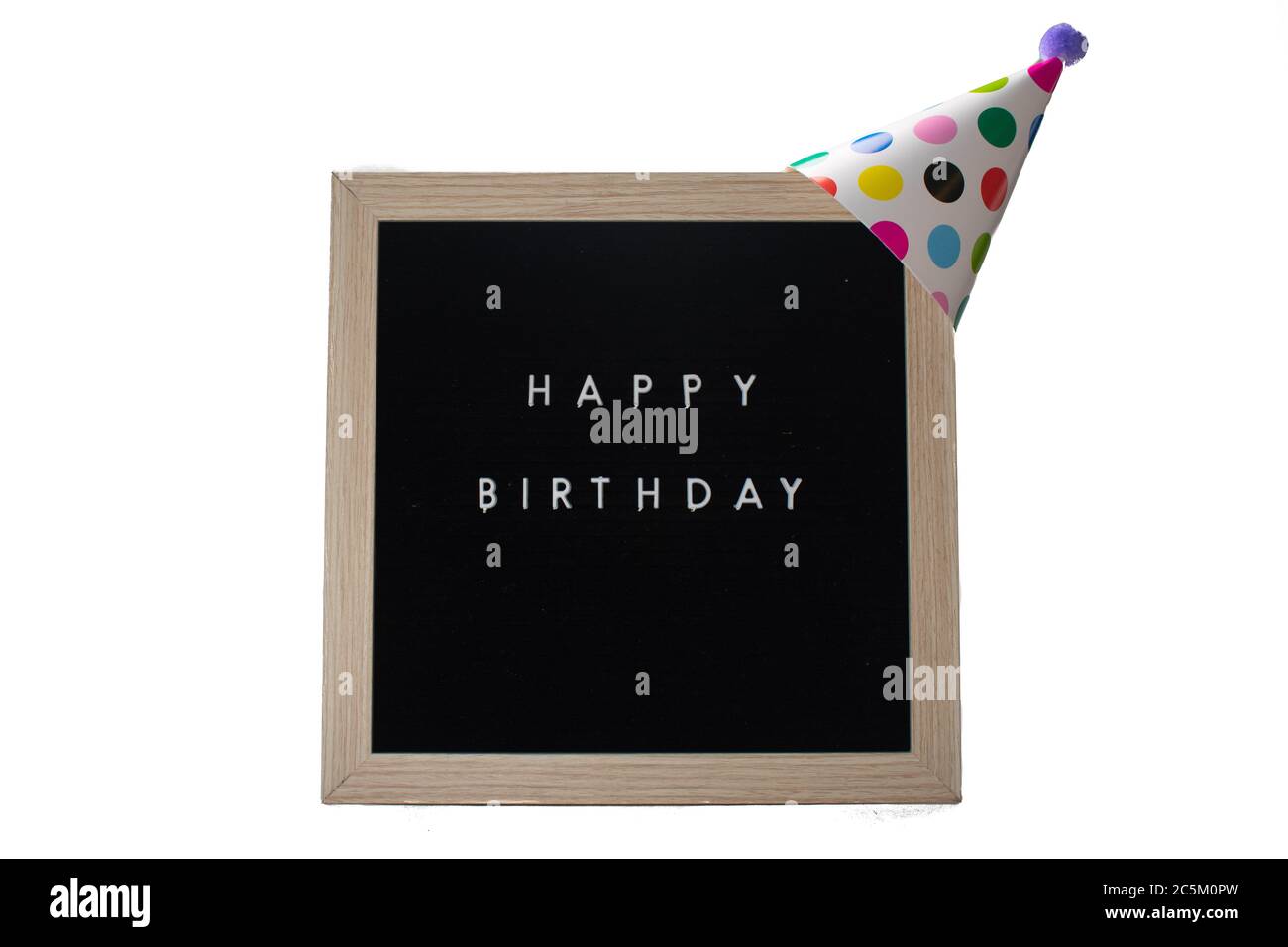 A Black Sign With a Birch Frame That Says Happy Birthday With a White Polka-Dotted Birthday Hat and a Purple Cotton Ball on Top on a Pure White Backgr Stock Photo