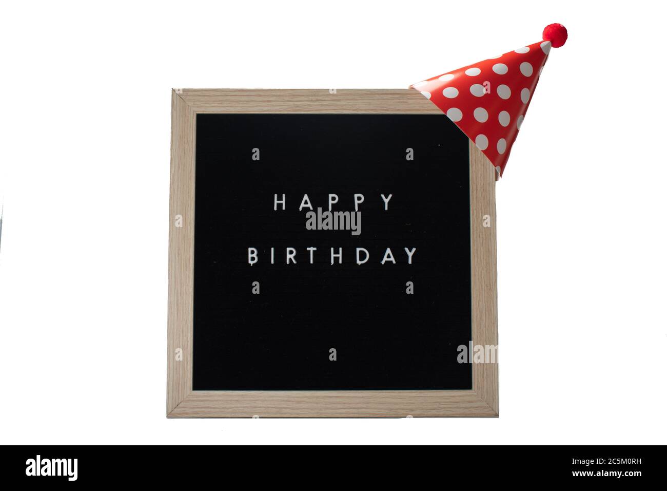 A Black Sign With a Birch Frame That Says Happy Birthday With a Red Polka-Dotted Birthday Hat and a Red Cotton Ball on Top on a Pure White Background Stock Photo