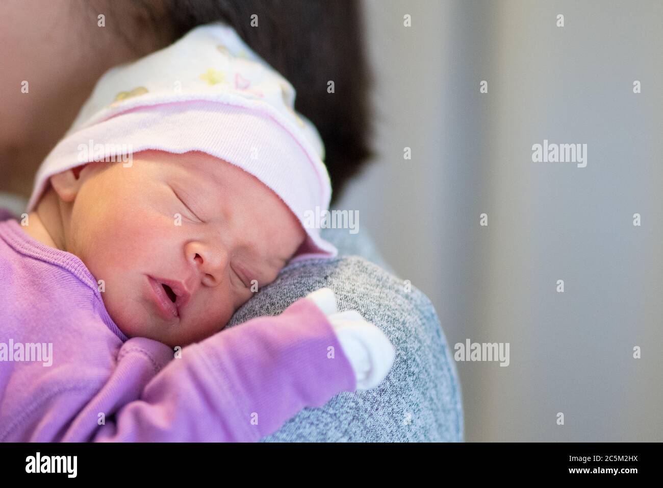 Mom holds her one month old baby girl on the shoulder while she is sleeping. Stock Photo