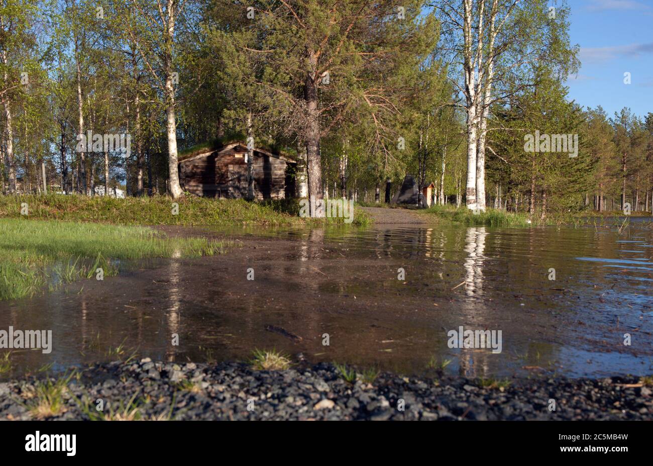View of a flooded country road, forest in the background. Wooden barn in the wood. Sunshine. Stock Photo
