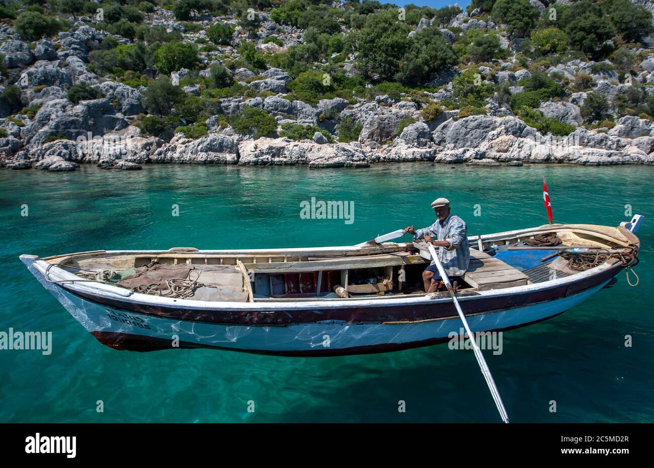 A Turkish man rows his boat through the turquoise water adjacent to Kekova Island in Turkey. Stock Photo