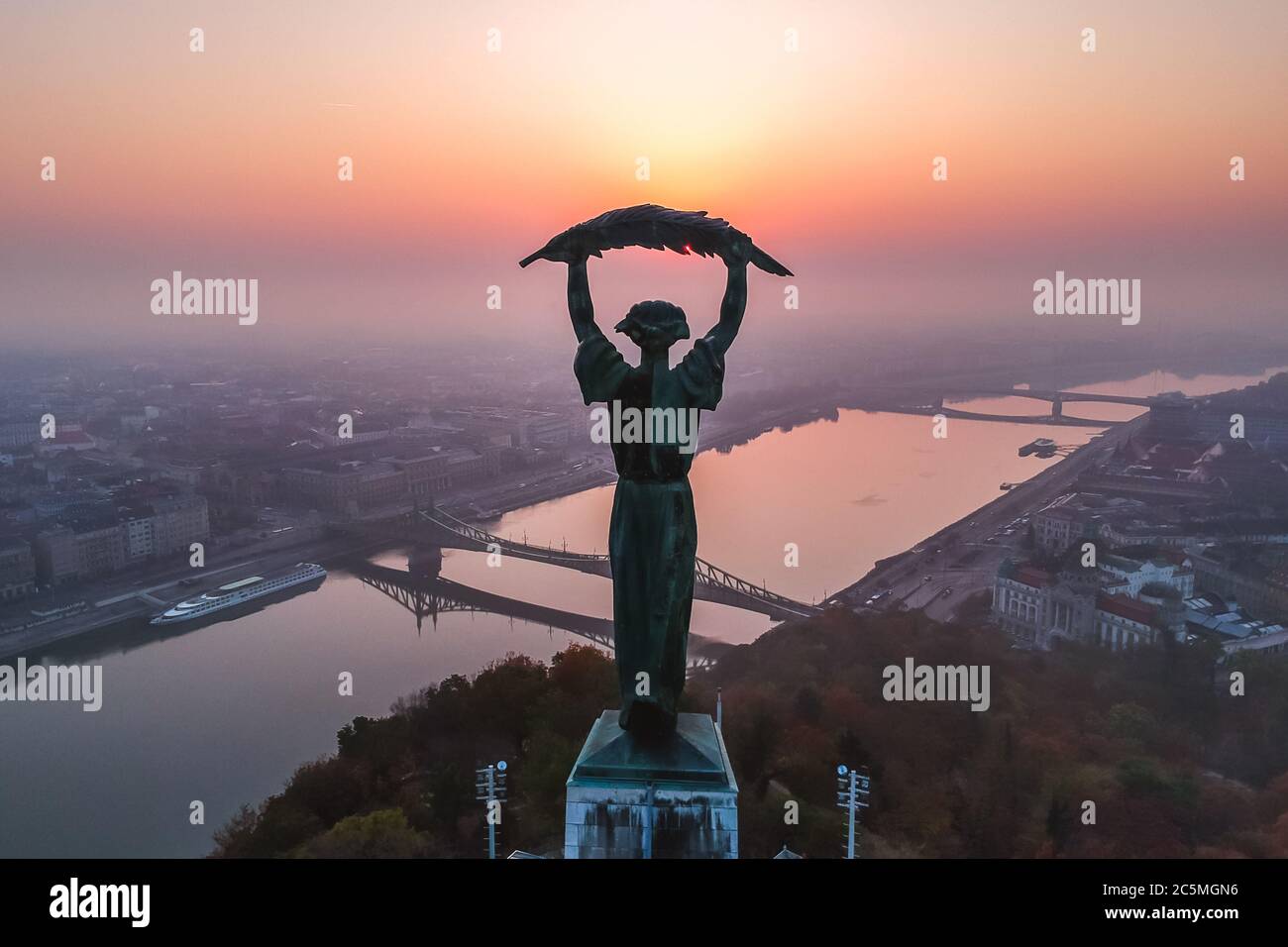 Aerial view to the Statue of Liberty with Liberty Bridge and River Danube at background taken from Gellert Hill on sunrise in fog in Budapest, Hungary Stock Photo