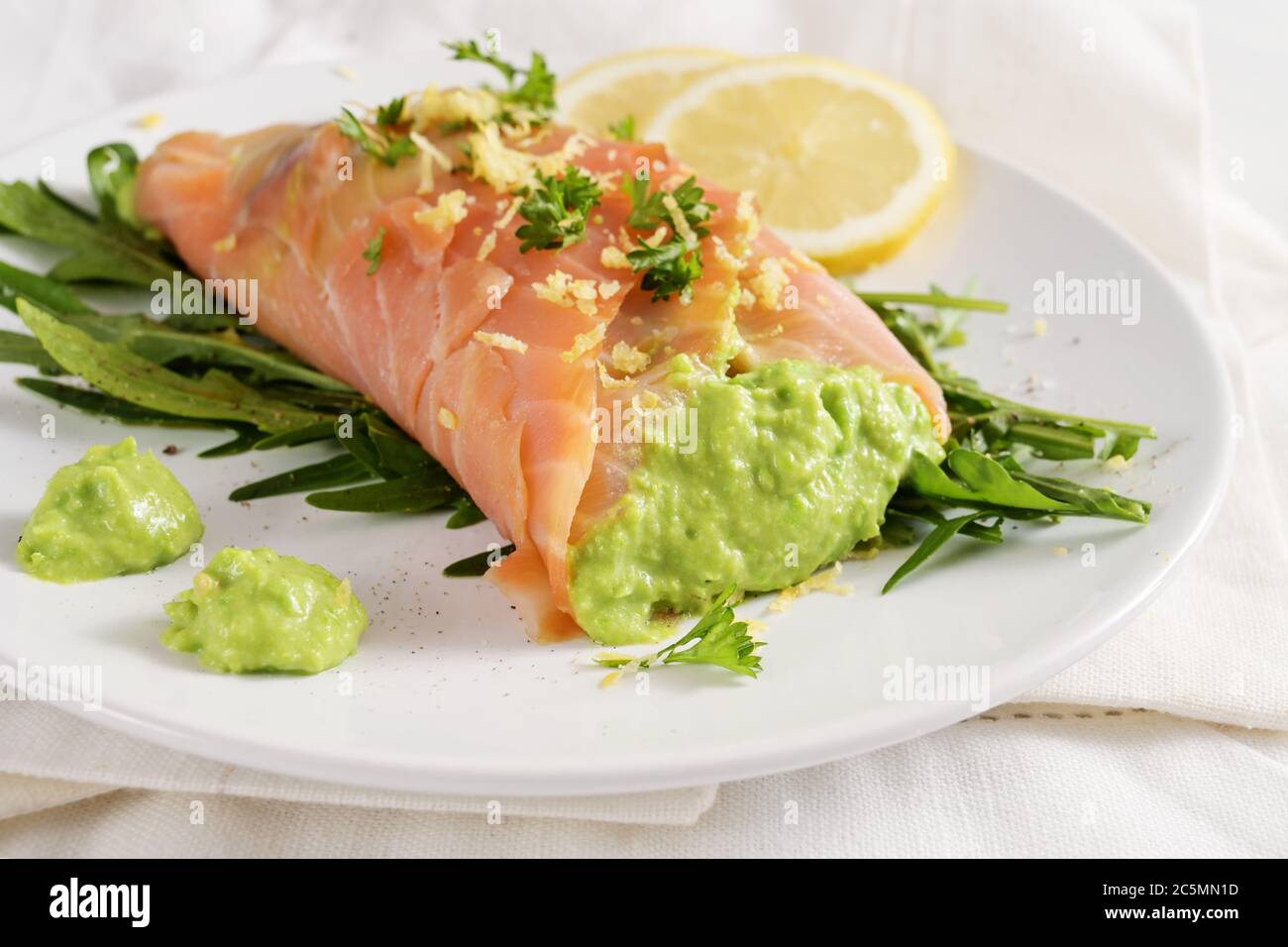 Salmon roll filled with pea puree on rocket salad with lemon slices and herb garnish on a white plate, low carb meal, selected focus, narrow depth of Stock Photo