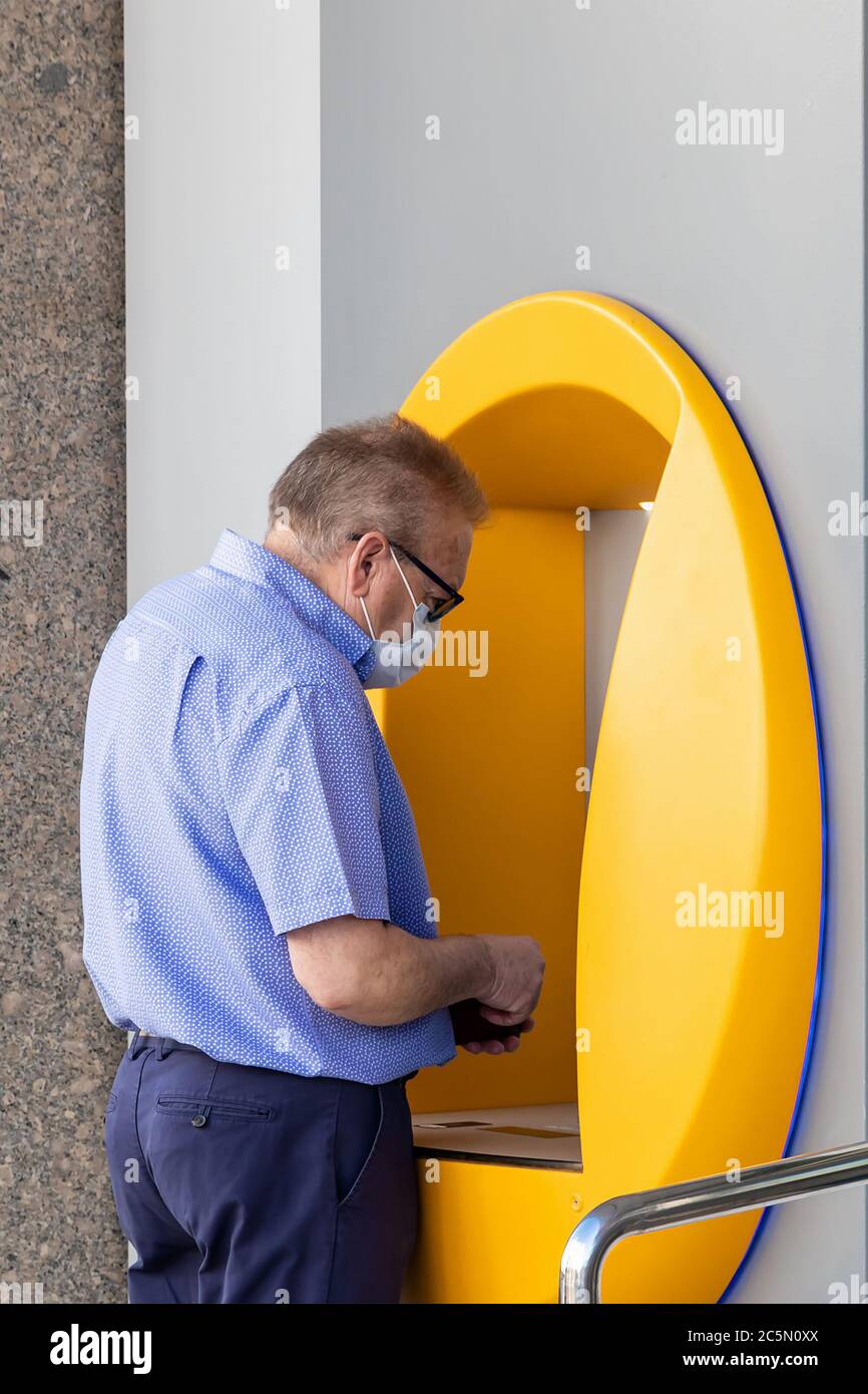 Punta Umbria, Huelva, Spain - June 3, 2020: Senior man using bank credit card in ATM machine is wearing a protective face mask due to covid-19 coronav Stock Photo