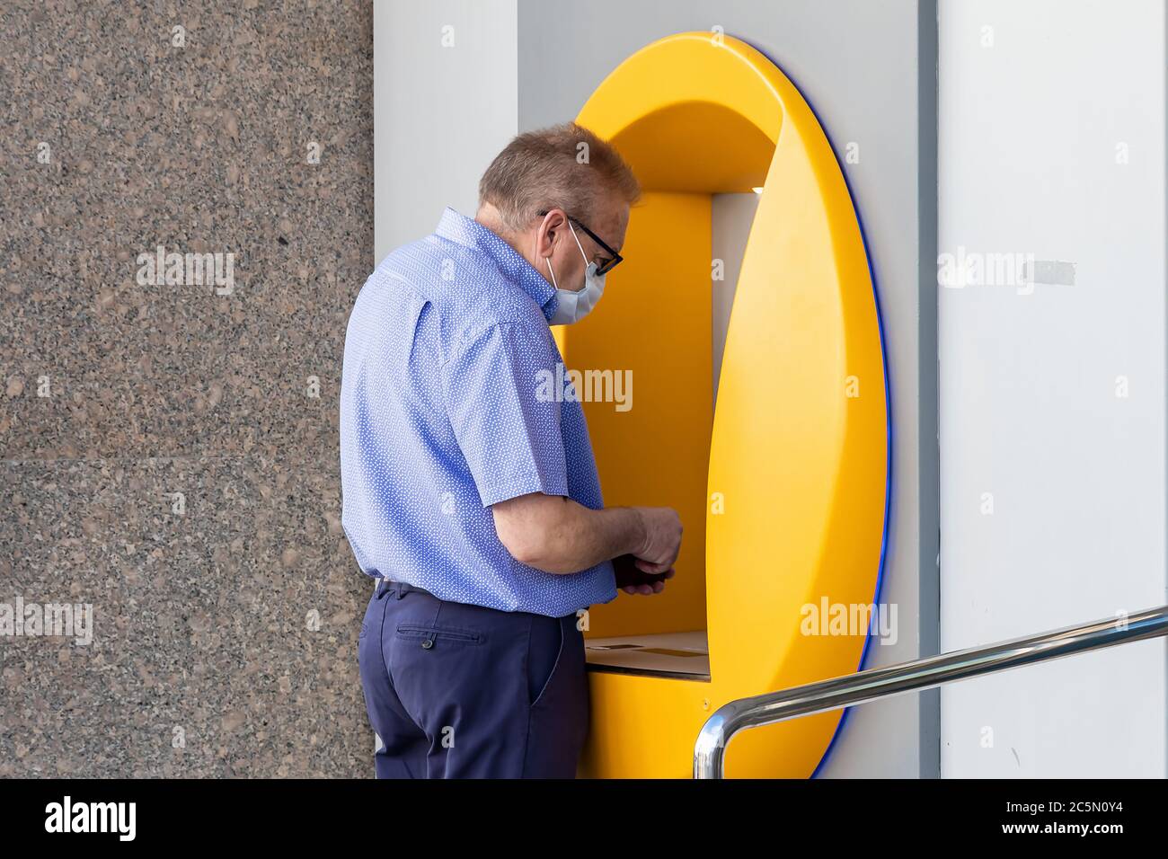 Punta Umbria, Huelva, Spain - June 3, 2020: Senior man using bank credit card in ATM machine is wearing a protective face mask due to covid-19 coronav Stock Photo