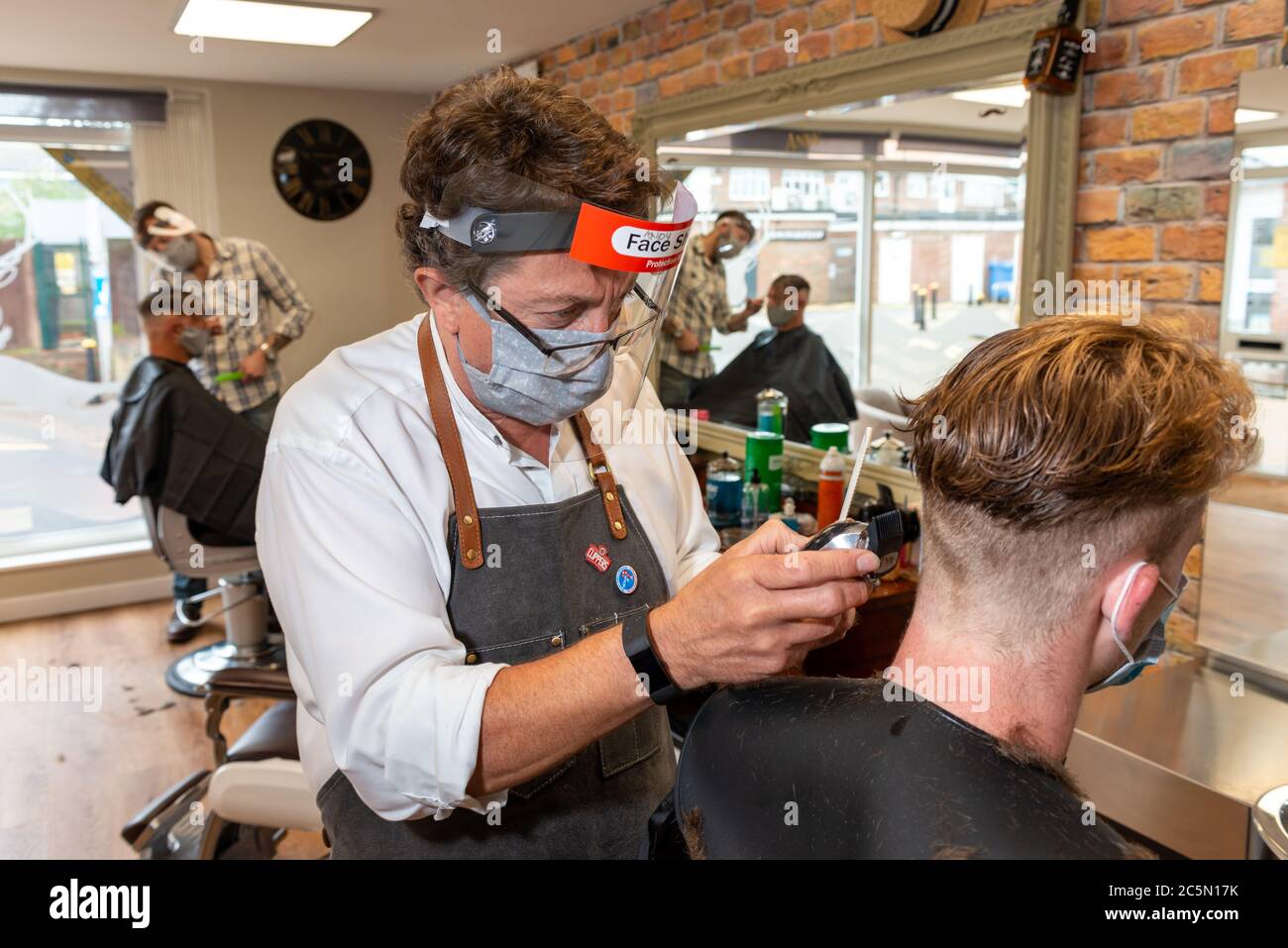 Rustington, Sussex, UK, 4th July 2020. As COVID-19 restrictions start to be lifted, today barbers are allowed to reopen. In Photo: Andy Cooper, Owner of Clipper Street Barbers, wears a facemask, face shield visor and PPE as he cuts the hair of one of his first customers on the day his business reopens. Credit: Scott Ramsey/Alamy Live News. Stock Photo