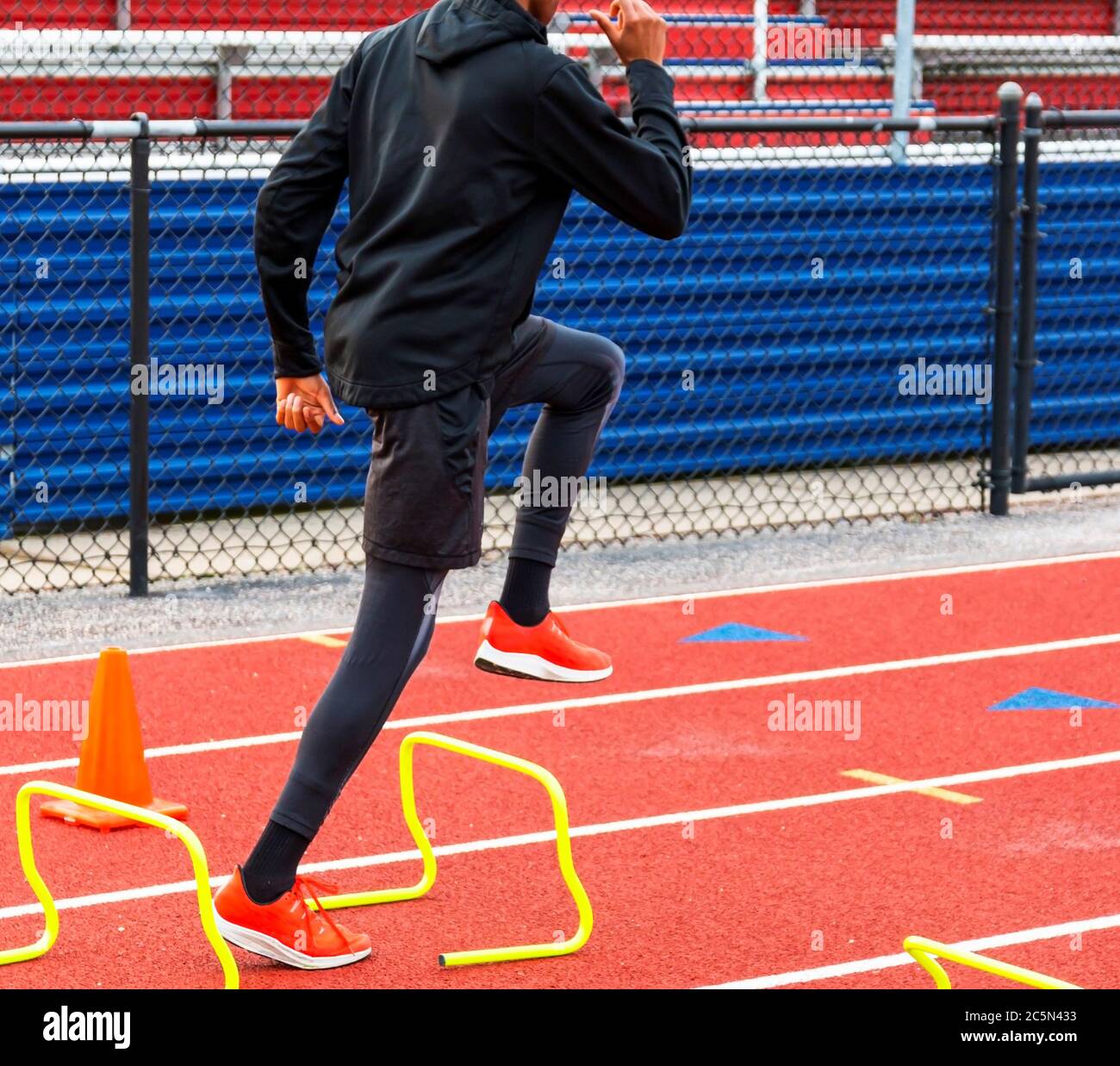 A high school track runner is stepping over yellow mini hurdles during speed and agility workout. Stock Photo