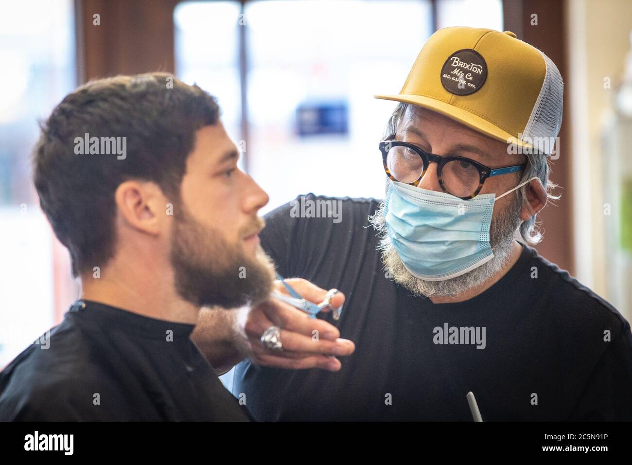 Barber cutting hair wearing PPE face mask at hair salon in early days of lockdown easing during Coronavirus pandemic. England July 2020 Stock Photo