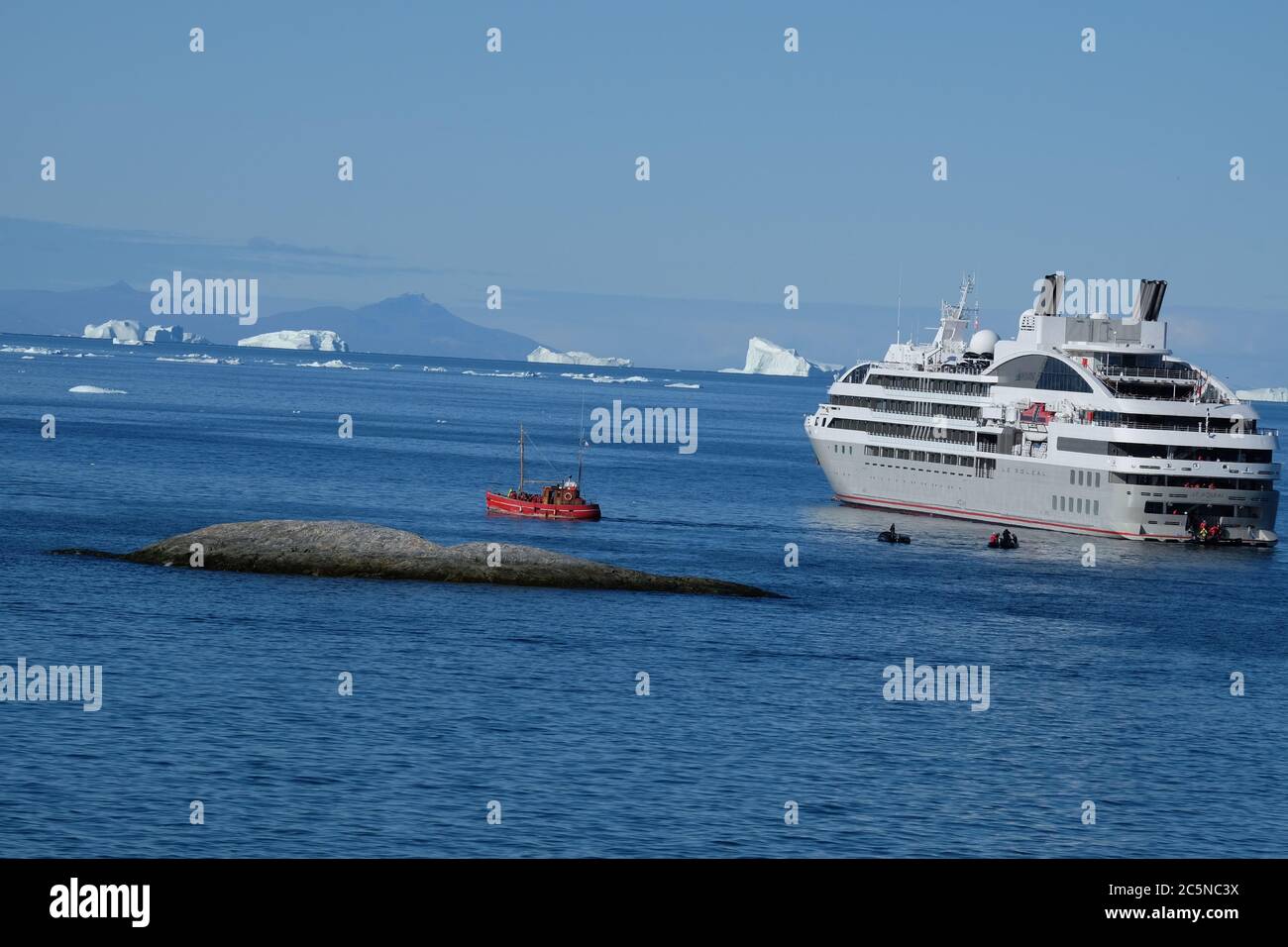 Little red fishing trawler stands by to board passengers from cruise liner for their memorable sail around giant icebergs. Stock Photo