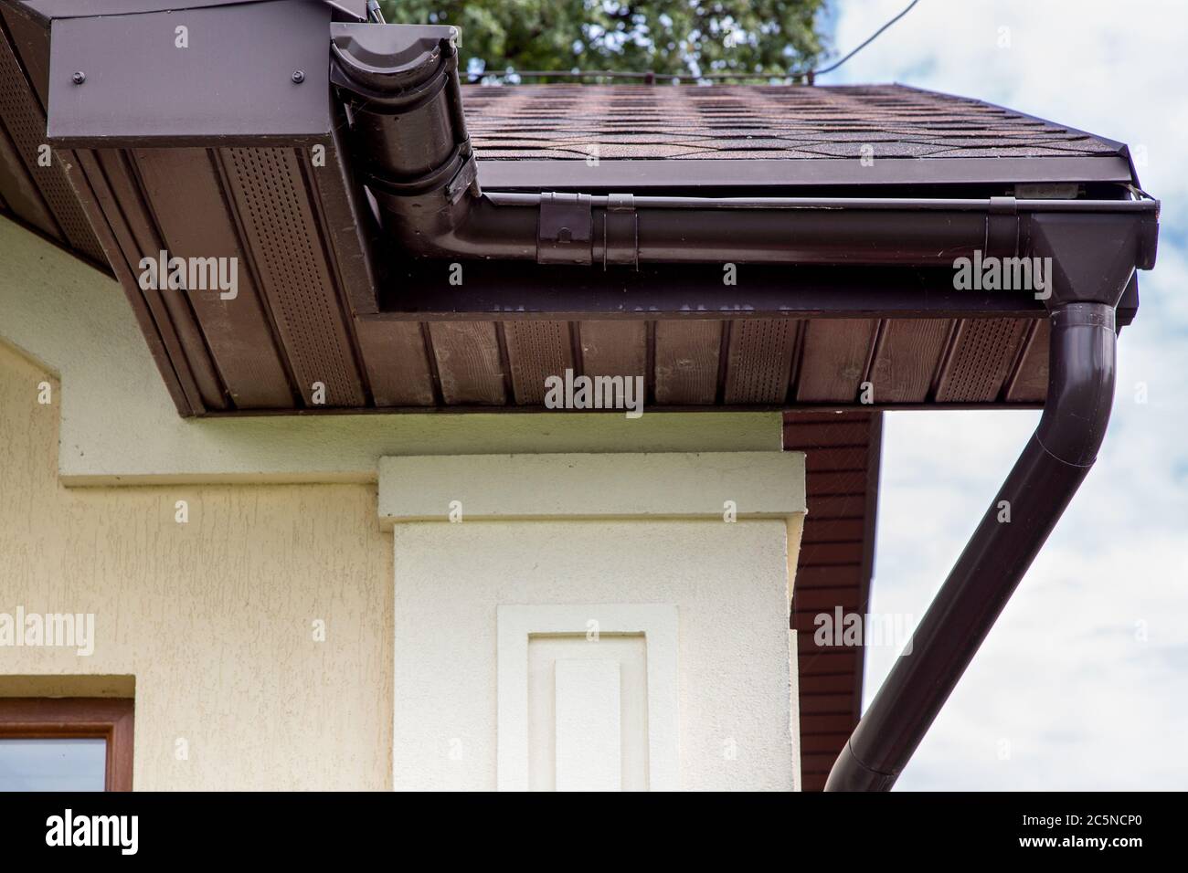 brown plastic drainage gutter on a roof with bituminous tiles close up