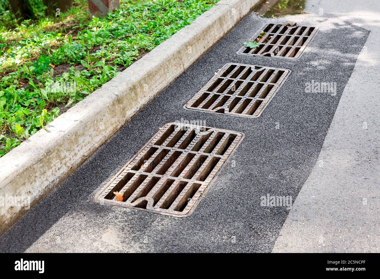 hatch storm system with a rusty grate in the asphalt road surface with a stone curb. Stock Photo