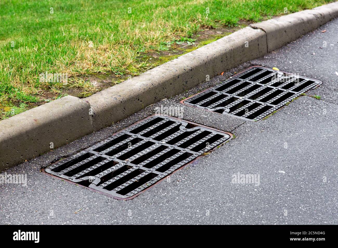 manhole cover rain grate on an asphalt road near a stone curb on the side of the road green grass. Stock Photo