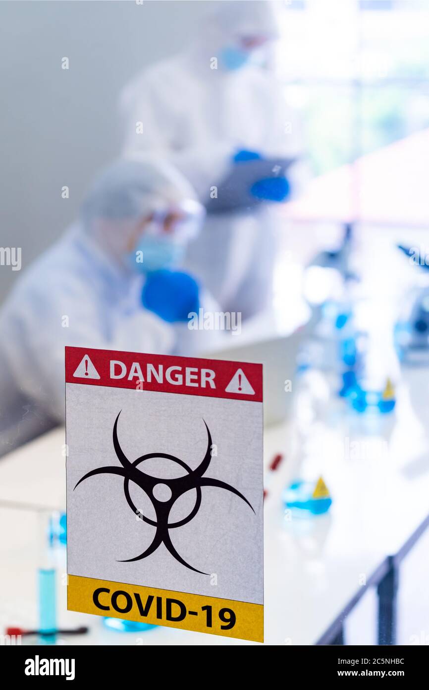 Caution danger Signage of COVID-19 coronavirus in front of Laboratory room with background of Scientists working and researching vaccine for ncov-19 v Stock Photo